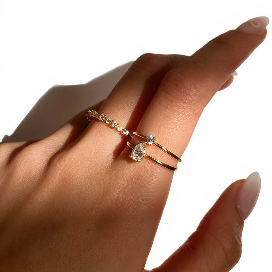 Hand wearing two gold rings with gemstones on a white background