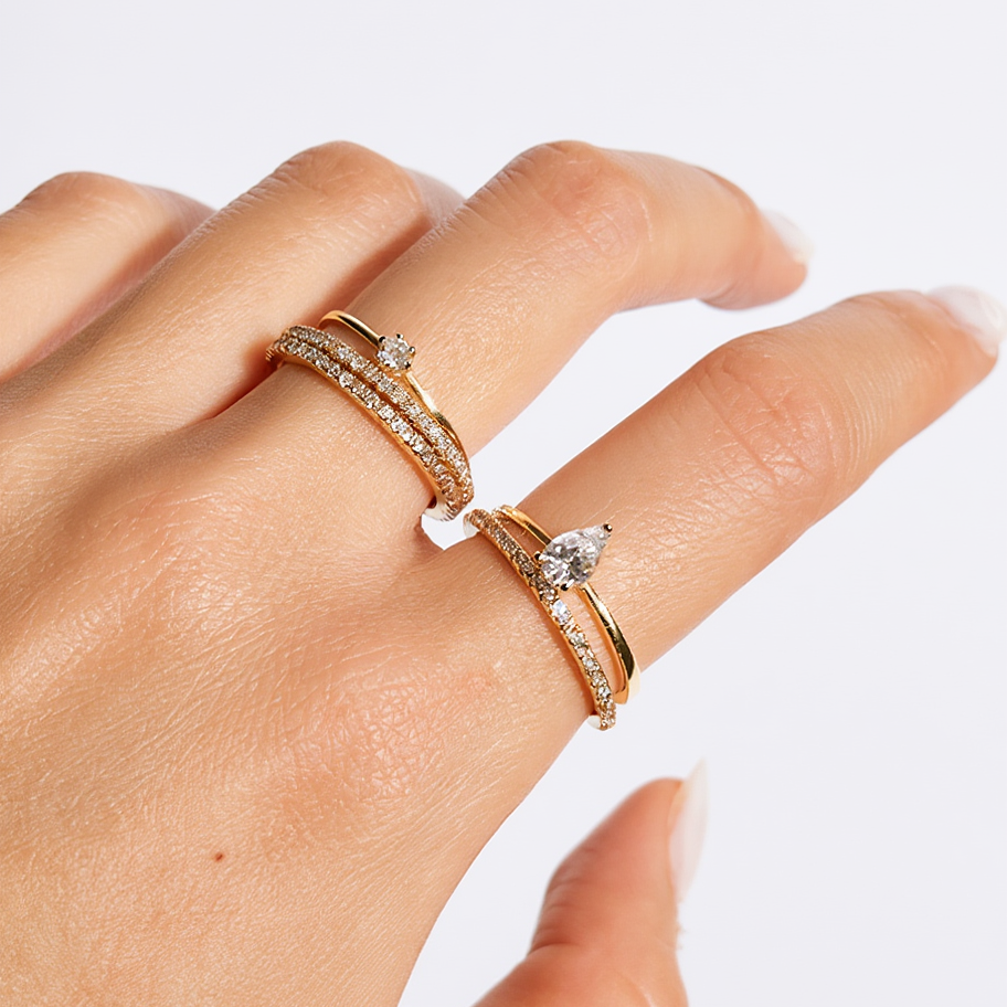 Hand wearing two gold rings with diamond accents on a light background